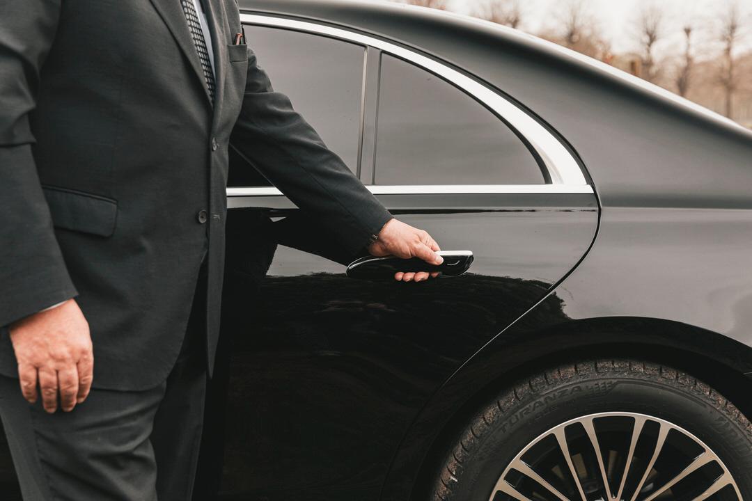 Le chauffeur garde ouverte la porte d’une Mercedes Classe S.